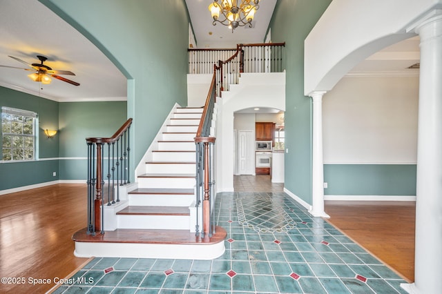 foyer featuring ceiling fan with notable chandelier, crown molding, dark hardwood / wood-style floors, a towering ceiling, and decorative columns