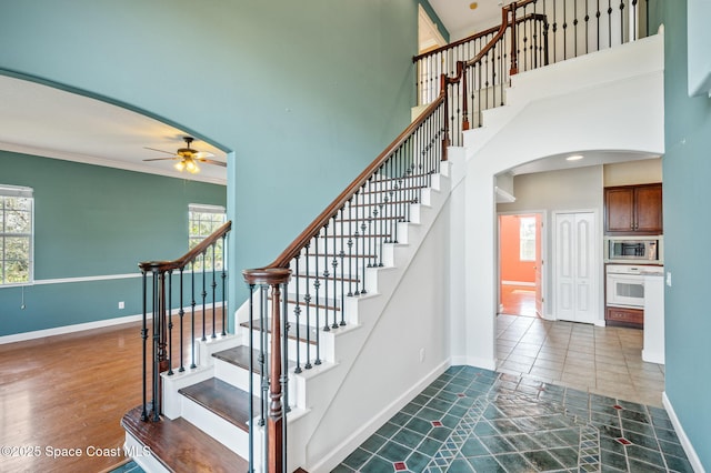 stairs with crown molding, ceiling fan, and a high ceiling