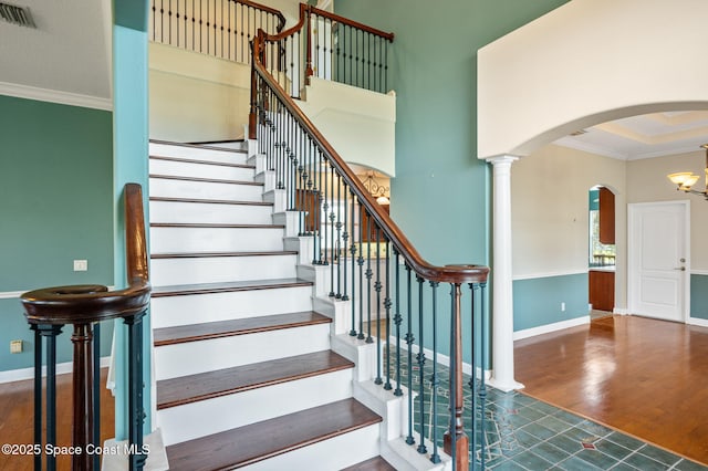 staircase with decorative columns, crown molding, and wood-type flooring