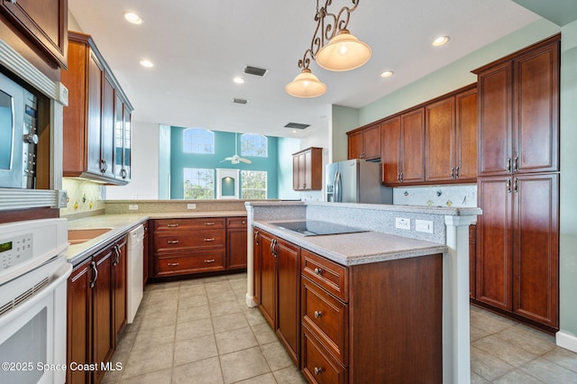 kitchen featuring white appliances, hanging light fixtures, tasteful backsplash, light stone counters, and kitchen peninsula