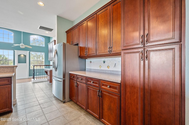 kitchen featuring ceiling fan, stainless steel fridge, decorative backsplash, light stone countertops, and light tile patterned floors