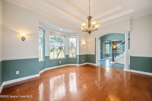 unfurnished room featuring ornate columns, an inviting chandelier, a raised ceiling, crown molding, and hardwood / wood-style floors