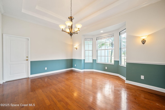 empty room featuring hardwood / wood-style flooring, a chandelier, ornamental molding, and a tray ceiling