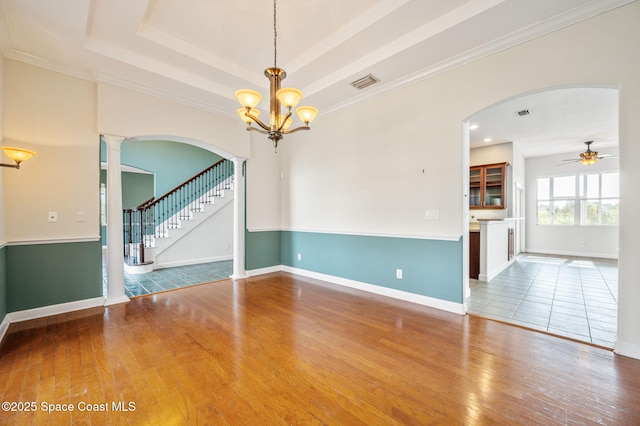 empty room featuring wood-type flooring, ceiling fan with notable chandelier, and ornamental molding