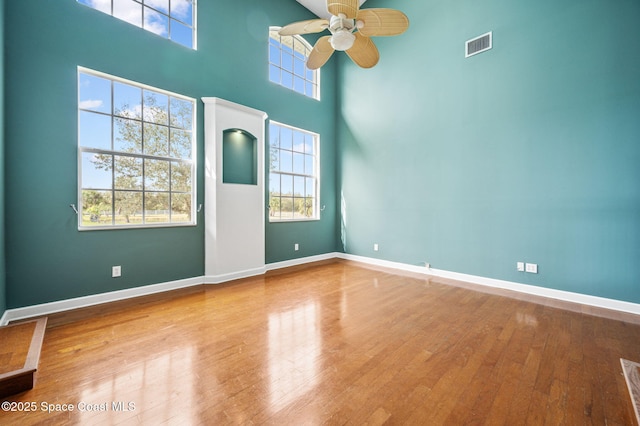 unfurnished room with ceiling fan, hardwood / wood-style floors, and a towering ceiling