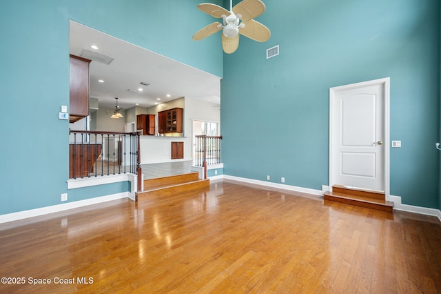 unfurnished living room with ceiling fan, a towering ceiling, and wood-type flooring