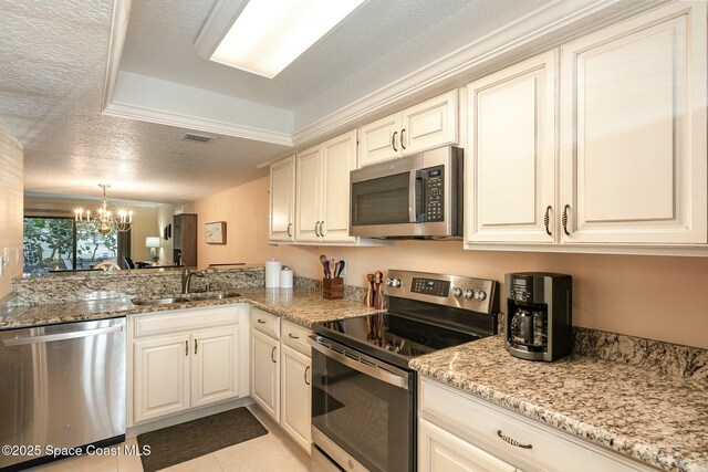 kitchen with stainless steel appliances, sink, a chandelier, light tile patterned floors, and a tray ceiling