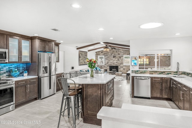 kitchen with stainless steel appliances, sink, vaulted ceiling with beams, ceiling fan, and decorative backsplash