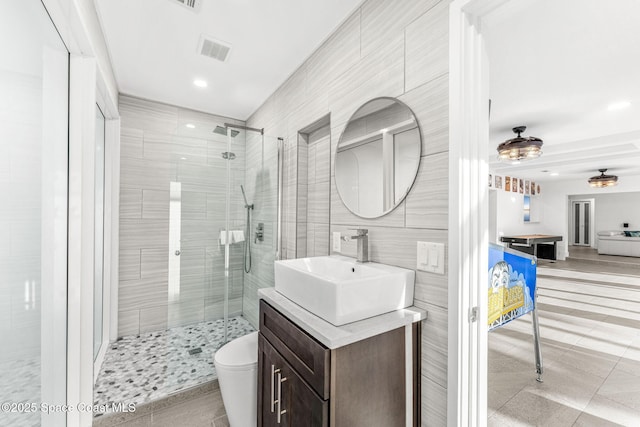 bathroom featuring toilet, tile walls, tile patterned floors, a shower with shower door, and vanity