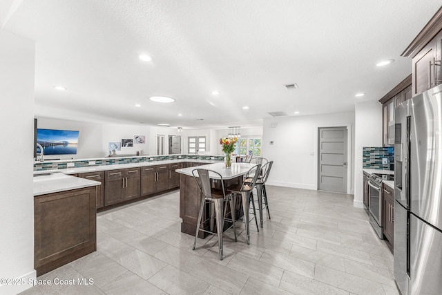 kitchen featuring kitchen peninsula, a center island, a breakfast bar, appliances with stainless steel finishes, and dark brown cabinets