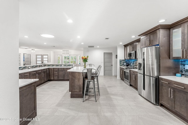 kitchen with stainless steel appliances, a kitchen island, a kitchen breakfast bar, and dark brown cabinets