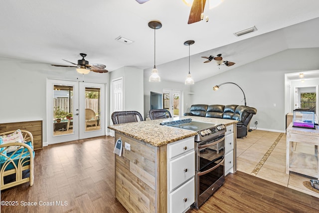 kitchen featuring a kitchen island with sink, range with two ovens, pendant lighting, french doors, and lofted ceiling