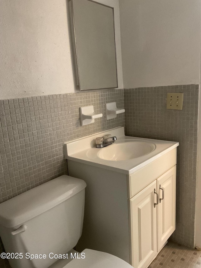 bathroom featuring tile patterned flooring, vanity, toilet, and tile walls