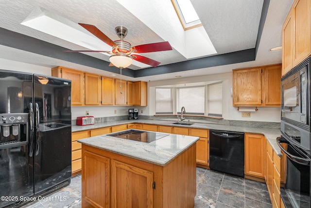 kitchen with a skylight, ceiling fan, a raised ceiling, black appliances, and a center island