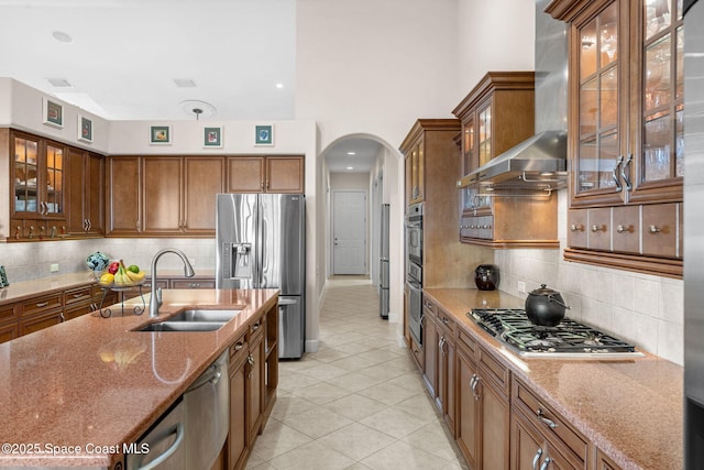 kitchen featuring stainless steel appliances, light stone countertops, sink, and wall chimney exhaust hood