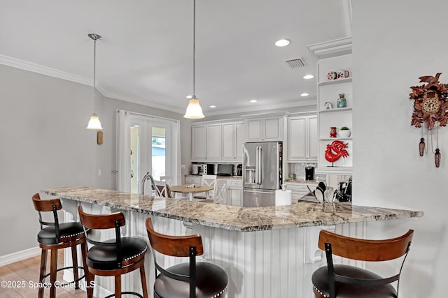 kitchen featuring pendant lighting, high quality fridge, a kitchen bar, tasteful backsplash, and kitchen peninsula