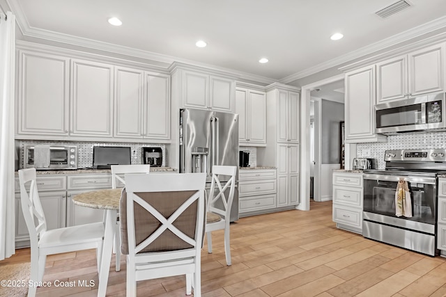 kitchen featuring white cabinetry, a kitchen bar, stainless steel appliances, ornamental molding, and a kitchen island