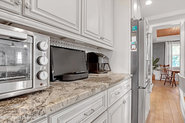 kitchen featuring light stone countertops, white cabinetry, stainless steel appliances, ornamental molding, and light hardwood / wood-style flooring