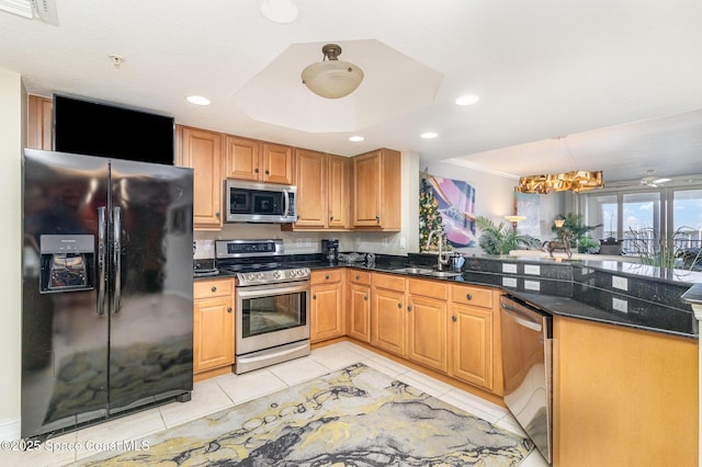 kitchen featuring appliances with stainless steel finishes, dark stone countertops, sink, light tile patterned floors, and a tray ceiling