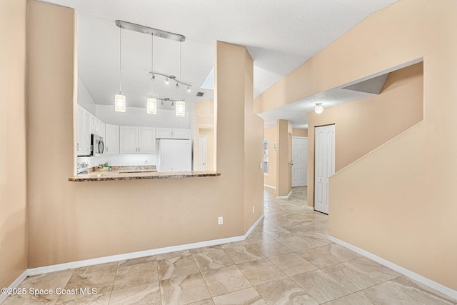 kitchen with kitchen peninsula, light stone counters, decorative light fixtures, white fridge, and white cabinetry