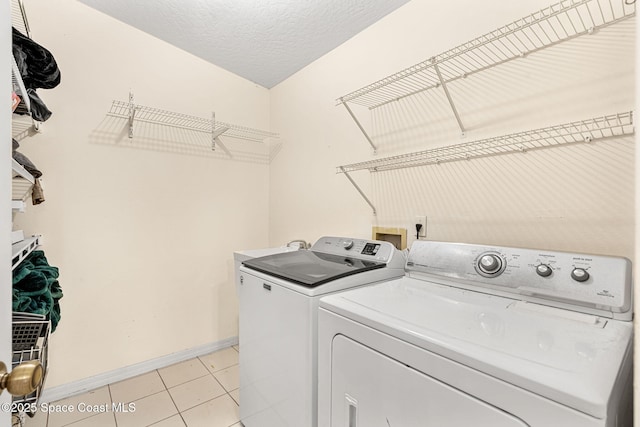 washroom featuring washing machine and clothes dryer, light tile patterned floors, and a textured ceiling