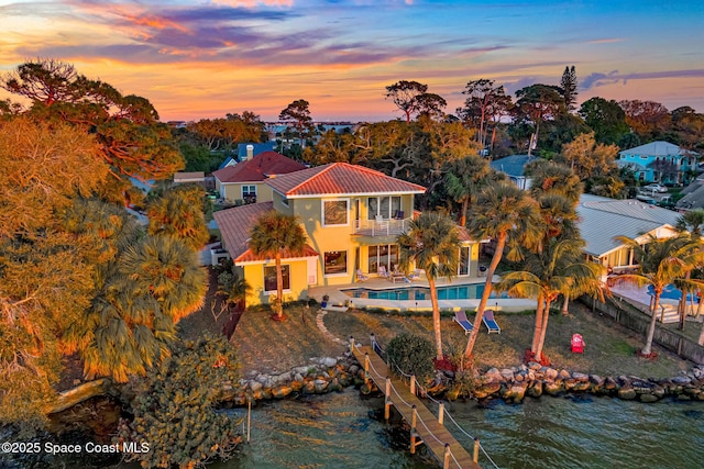 back house at dusk with a lawn, a balcony, a water view, and a patio