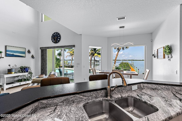 kitchen with a textured ceiling, sink, a water view, an inviting chandelier, and plenty of natural light