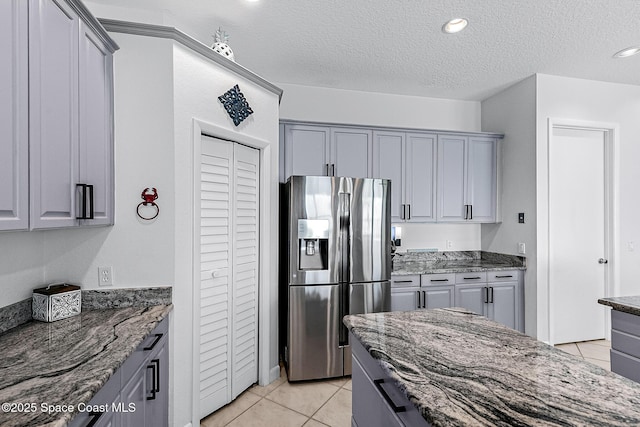 kitchen with a textured ceiling, light tile patterned flooring, dark stone countertops, and stainless steel refrigerator with ice dispenser