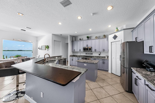 kitchen with gray cabinetry, sink, a kitchen island, a water view, and appliances with stainless steel finishes