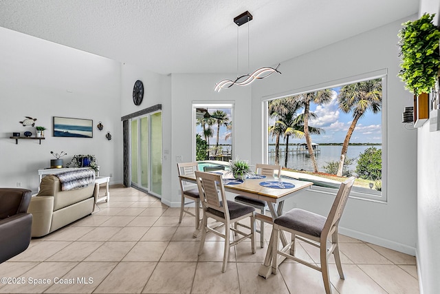 dining area featuring a textured ceiling, a water view, and light tile patterned flooring