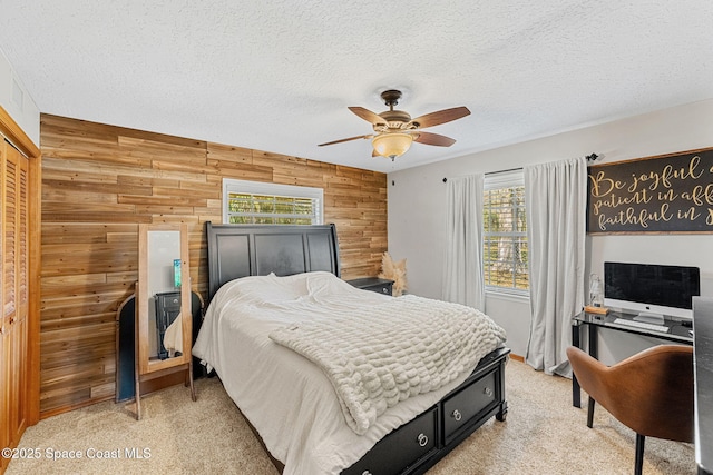 bedroom featuring ceiling fan, light carpet, a textured ceiling, and wood walls