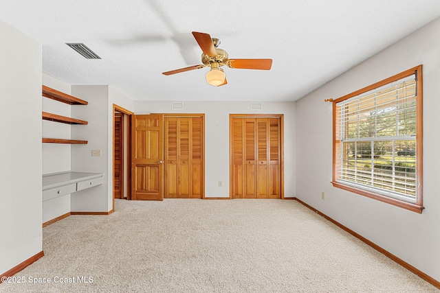 unfurnished bedroom with multiple closets, light colored carpet, built in desk, and a textured ceiling