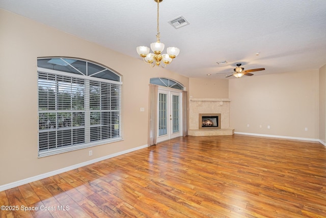 unfurnished living room with hardwood / wood-style flooring, a high end fireplace, a textured ceiling, ceiling fan with notable chandelier, and french doors