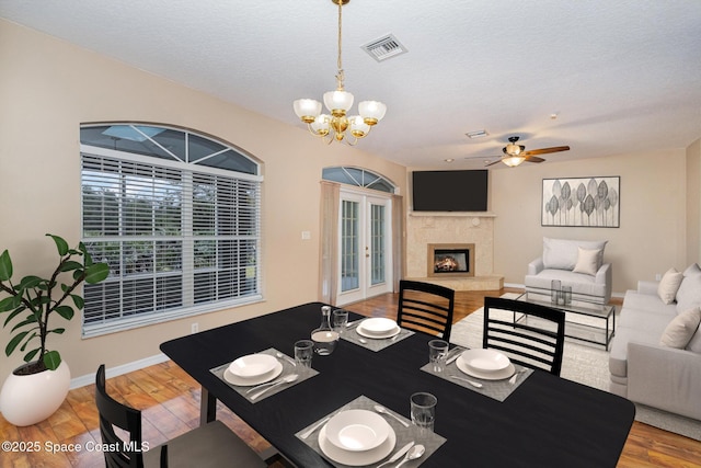 dining area featuring french doors, a premium fireplace, ceiling fan with notable chandelier, and light wood-type flooring