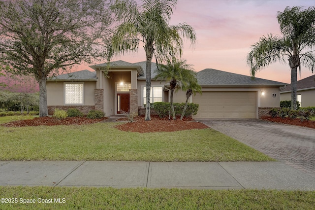 view of front of home with decorative driveway, an attached garage, stucco siding, and a front yard