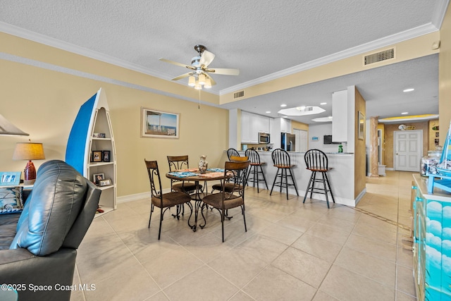 tiled dining room featuring a textured ceiling, ornamental molding, and ceiling fan