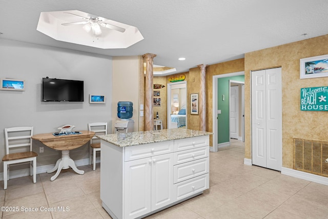 kitchen with light tile patterned floors, ceiling fan, light stone counters, a kitchen island, and white cabinets