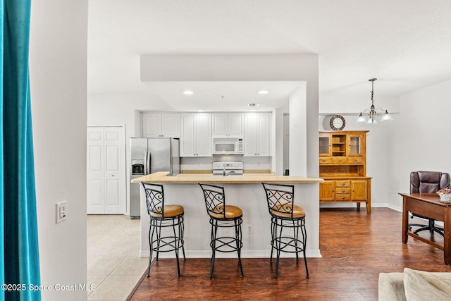 kitchen featuring a kitchen bar, white cabinetry, range, stainless steel fridge, and pendant lighting