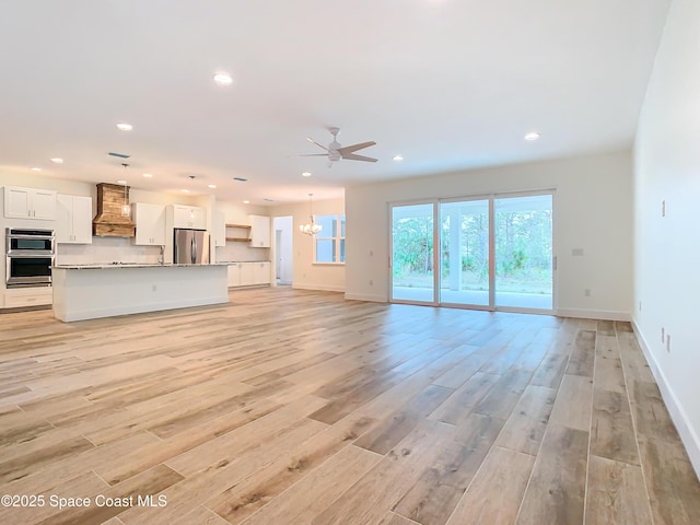 unfurnished living room with ceiling fan with notable chandelier and light hardwood / wood-style floors