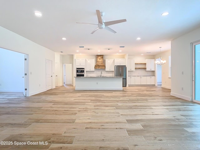 kitchen featuring premium range hood, a center island with sink, appliances with stainless steel finishes, hanging light fixtures, and white cabinets