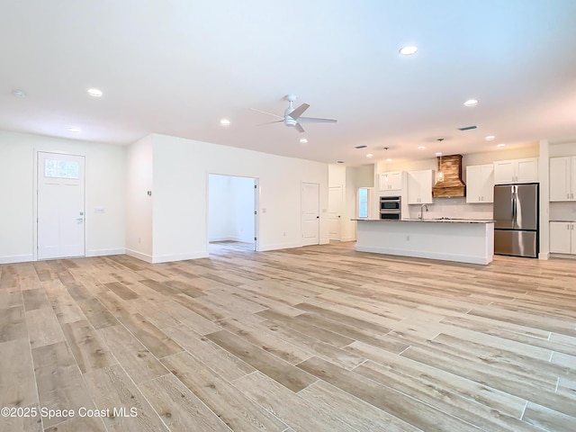 unfurnished living room with ceiling fan, sink, and light hardwood / wood-style flooring