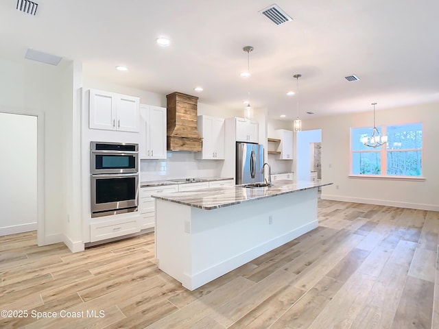 kitchen featuring white cabinets, appliances with stainless steel finishes, hanging light fixtures, a kitchen island with sink, and a notable chandelier