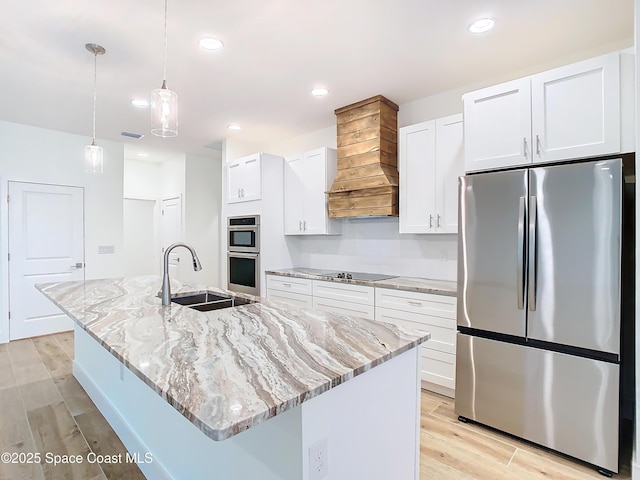 kitchen with pendant lighting, white cabinets, stainless steel appliances, an island with sink, and custom range hood