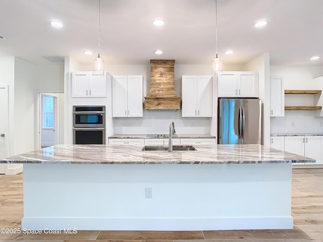 kitchen with custom exhaust hood, a kitchen island with sink, appliances with stainless steel finishes, and white cabinetry