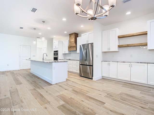 kitchen featuring hanging light fixtures, stainless steel appliances, custom range hood, white cabinets, and stone countertops