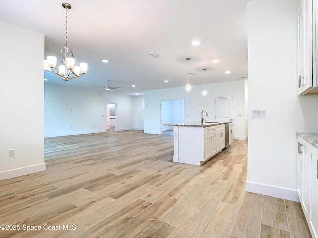 kitchen with an island with sink, ceiling fan with notable chandelier, white cabinetry, and pendant lighting