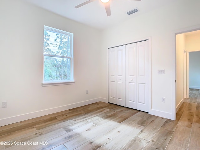 unfurnished bedroom with light wood-type flooring, ceiling fan, and a closet