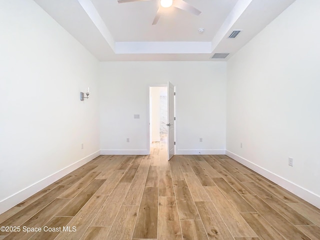 empty room with ceiling fan, light hardwood / wood-style flooring, and a raised ceiling