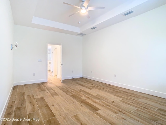 empty room with ceiling fan, light hardwood / wood-style floors, and a raised ceiling