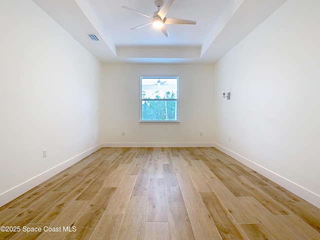 spare room with ceiling fan, a tray ceiling, and light hardwood / wood-style flooring